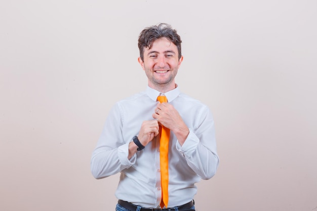 Young man adjusting his tie in shirt, jeans and looking happy