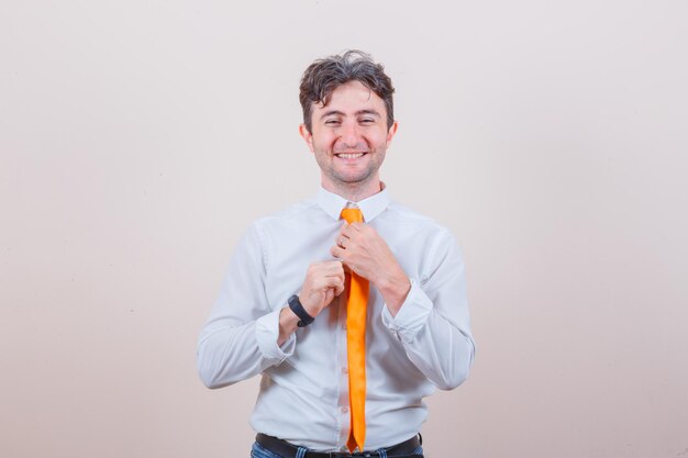 Young man adjusting his tie in shirt, jeans and looking happy