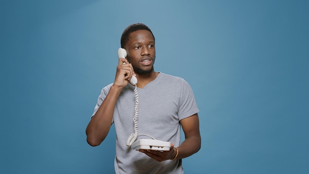 Free photo young man answering landline phone call in studio, having remote conversation on office telephone with cable. person having discussion on telework communication device, with wired cord.