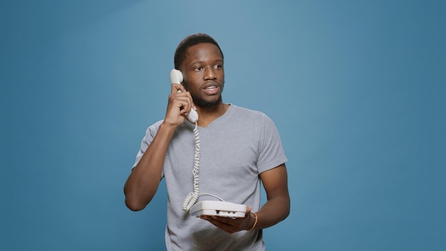 Young man answering landline phone call in studio, having remote conversation on office telephone with cable. Person having discussion on telework communication device, with wired cord.