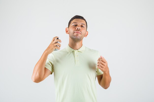 Young man applying perfume on his neck in t-shirt front view.