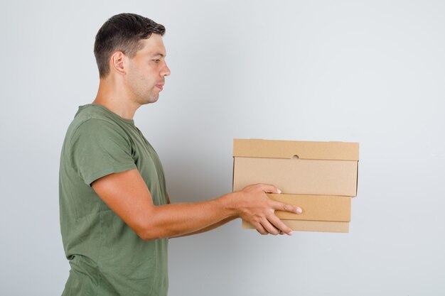 Young man in army green t-shirt holding cardboard boxes .