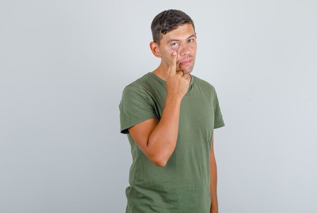 손가락, 전면보기와 아래쪽 뚜껑에 눈을 당기는 육군 녹색 티셔츠에 젊은 남자.
