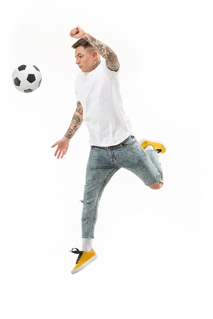 白い背景の上のスタジオでジャンプしてボールを蹴るサッカーサッカー選手としての若い男。