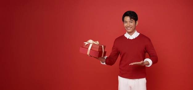 アジア系の若い男性が赤いスウェットを着てギフトリボンボウ付きの赤いプレゼントボックスを握っています
