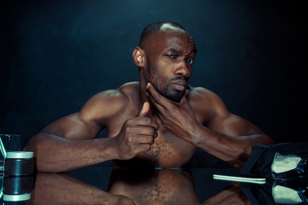 Young man in bedroom sitting in front of the mirror after scratching his beard