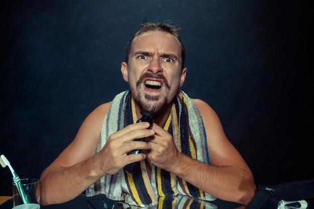  young man in bedroom sitting in front of  mirror scratching his beard at home. Human emotions and lifestyle concept