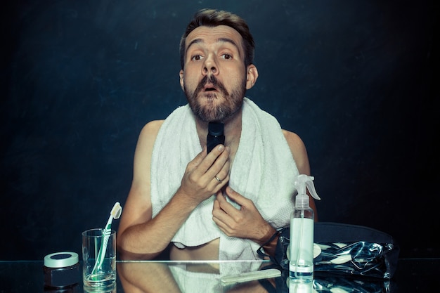 The young man in bedroom sitting in front of the mirror scratching his beard at home