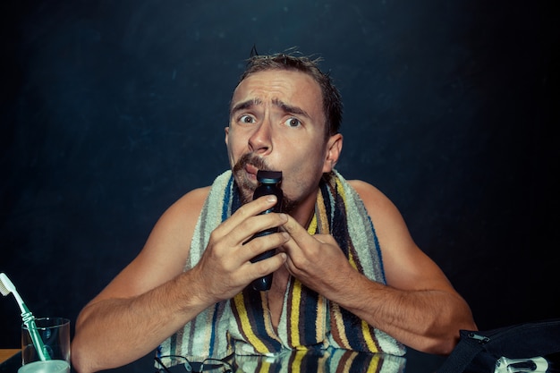 Free photo young man in bedroom sitting in front of the mirror scratching his beard