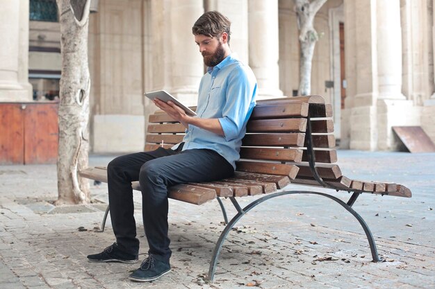 молодой человек на скамейке на улице с планшетом в руке
