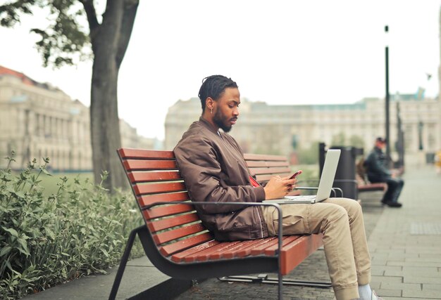 young man on a bench with a computer and a smartphone