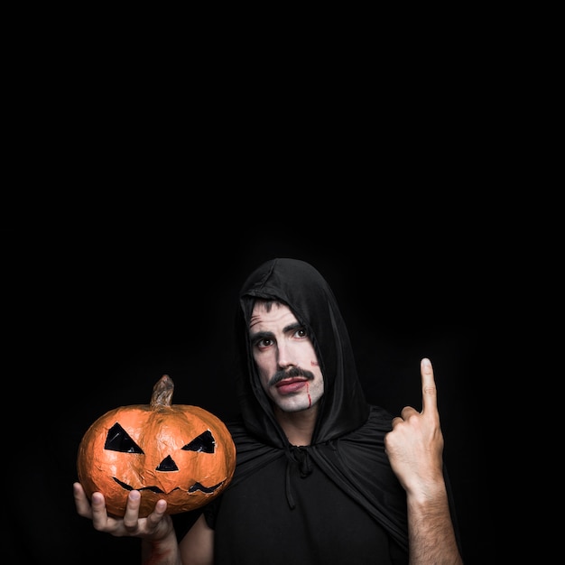 Free photo young man in black cloak posing in studio with halloween pumpkin