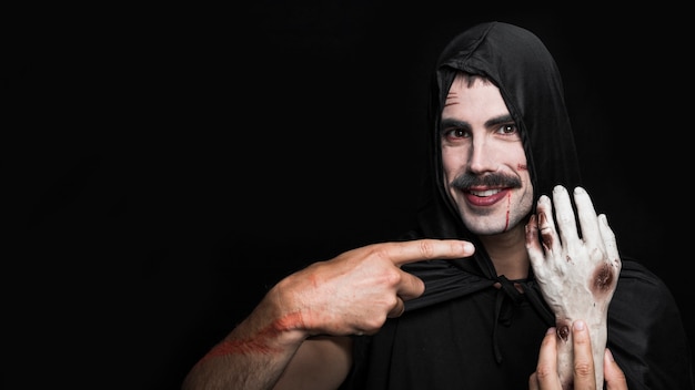 Free photo young man in black cloak showing artificial hand of corpse