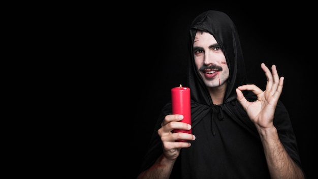 Young man in black cloak with candle making ok gesture