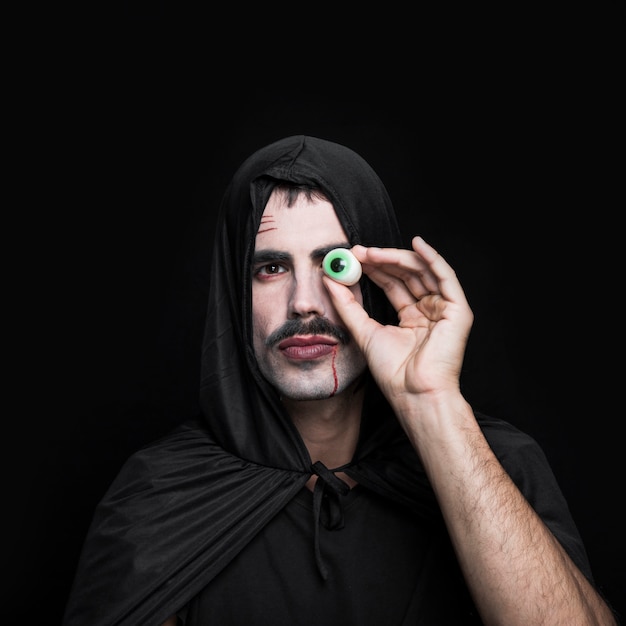 Young man in black cloak with hood holding artificial eye