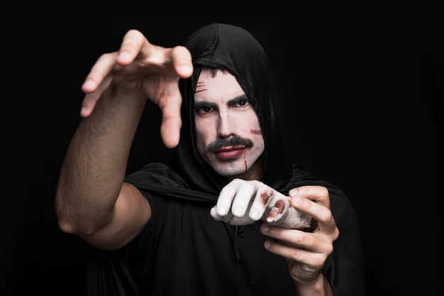 Young man in black clothes posing in studio with corpse hand