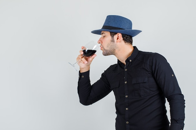 Giovane uomo in camicia nera, cappello di bere alcolici