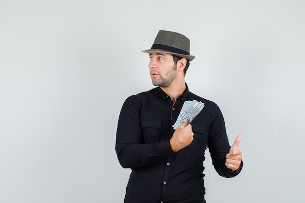 Young man in black shirt, hat holding money with finger sign