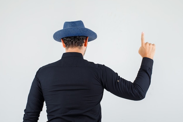 Giovane uomo in camicia nera, cappello rivolto verso l'alto e guardando fiducioso