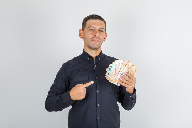 Young man in black shirt pointing finger at euro banknotes