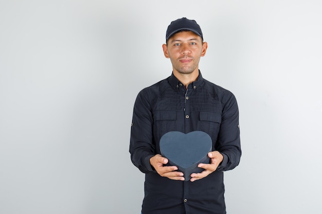 Giovane in camicia nera con cappuccio che tiene il contenitore di regalo e che sembra allegro