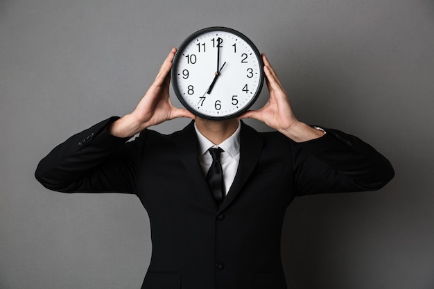 Free photo young man in black suit holding clock in front of his face