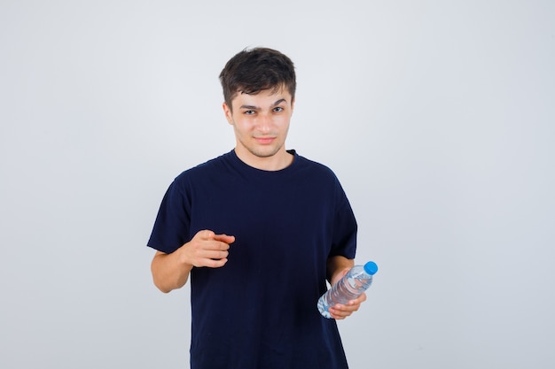 Молодой человек в черной футболке держит бутылку воды, указывая на камеру и выглядит разумно, вид спереди.