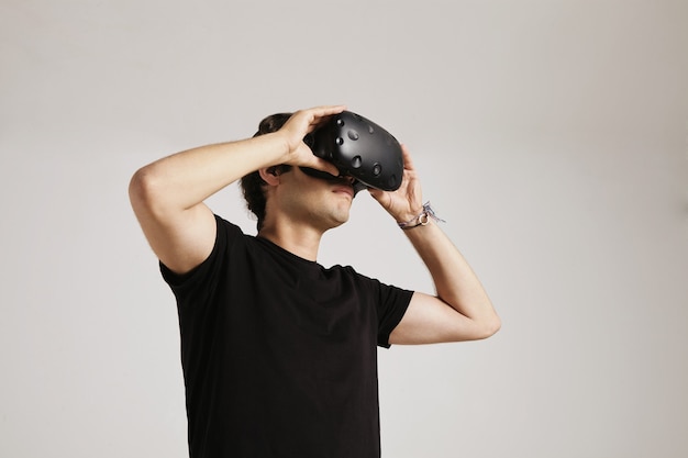 A young man in blank black t-shirt puts on VR glasses isolated on white