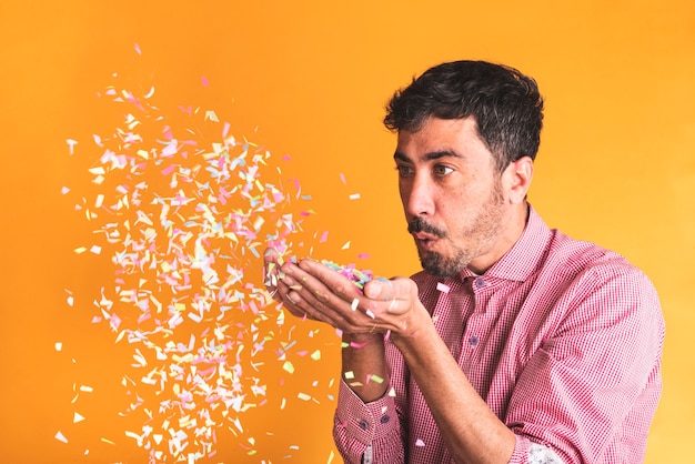 Free photo young man blowing confetti on orange background