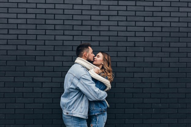 Молодой человек в синей джинсовой одежде, наслаждаясь свиданием в холодный день. Замечательная кавказская девушка целует парня с любовью.