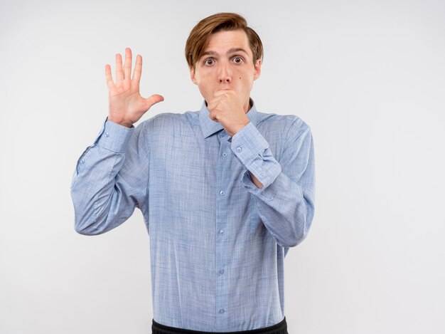 Young man in blue shirt  being confused raising palm standing over white wall