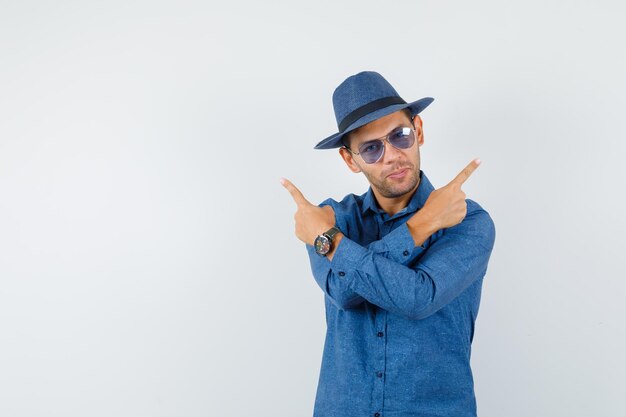 Young man in blue shirt, hat pointing away and looking confident , front view.