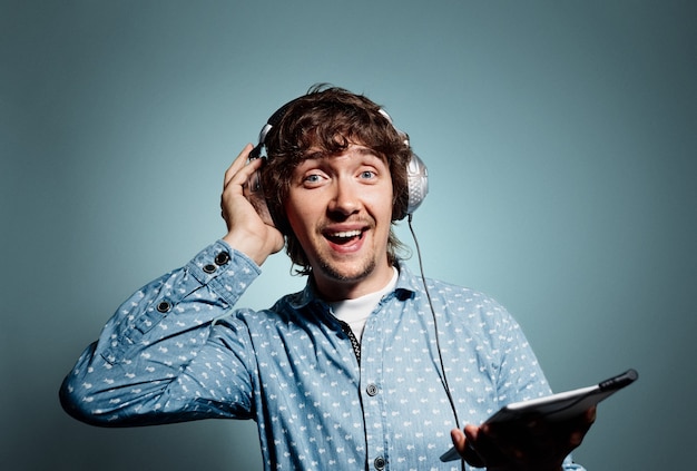 Young man in blue shirt holding tablet and wearing headphones