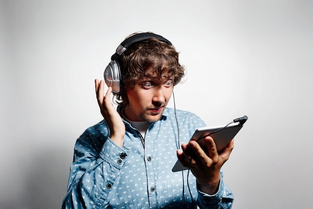 Young man in blue shirt holding tablet and wearing headphones