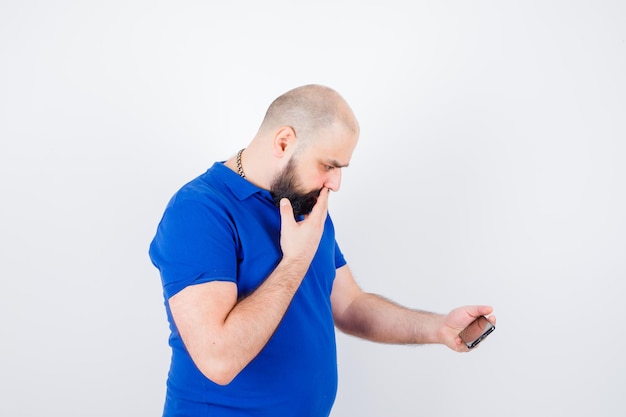 Foto gratuita giovane in camicia blu che guarda il telefono e sembra ansioso.