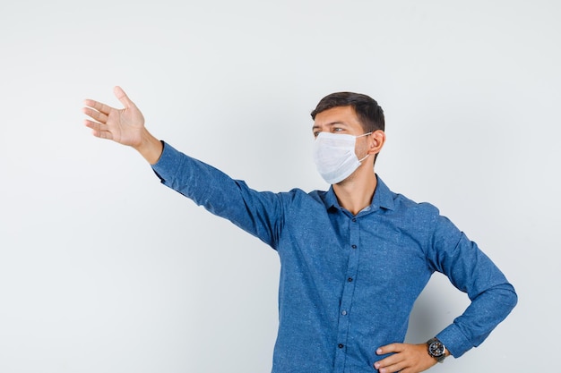 Young man in blue shirt, mask shouting to somebody while looking away , front view.