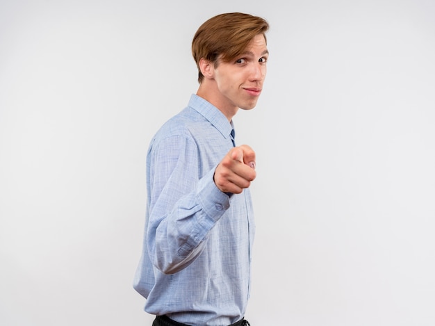 Молодой человек в синей рубашке указывая с уверенно улыбающимся указательным пальцем, стоящим над белой стеной
