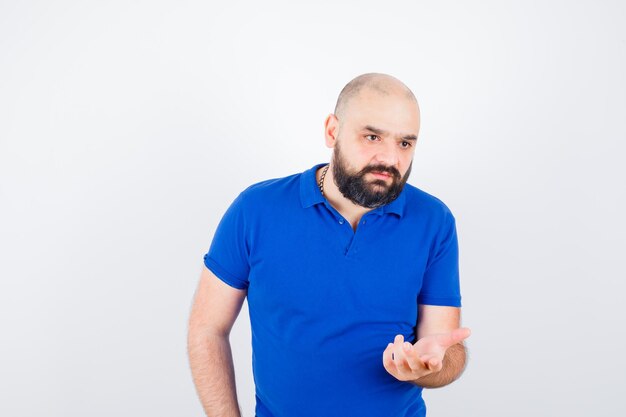 Young man in blue shirt raising hand up with open palm and looking displeased , front view.