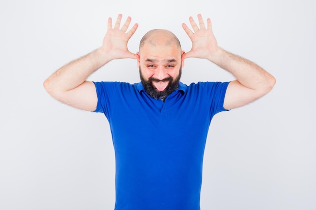 Young man in blue shirt showing horn sign while sticking tongue out and looking funny , front view.