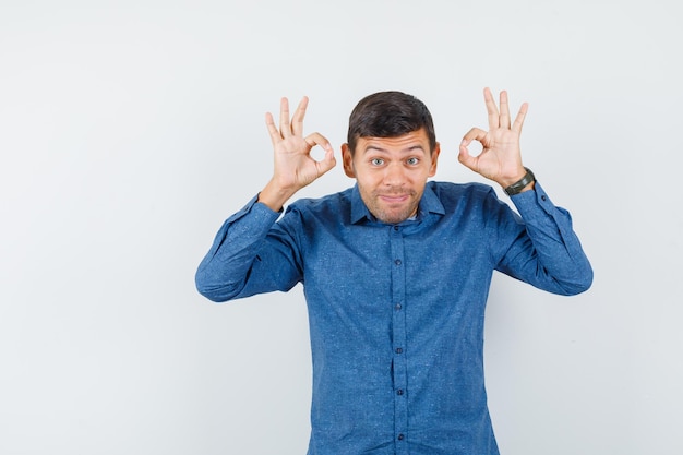 Young man in blue shirt showing ok sign and looking cheerful , front view.