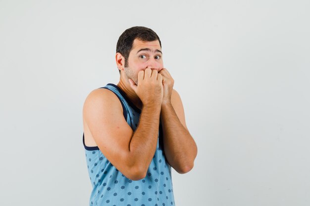 Young man in blue singlet biting fists emotionally and looking scared