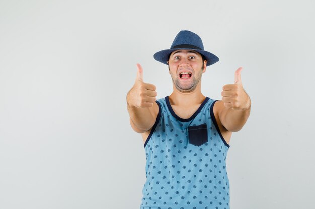 파란색 중항, 두 엄지 손가락을 보여주는 모자와 행복을 찾는 젊은 남자