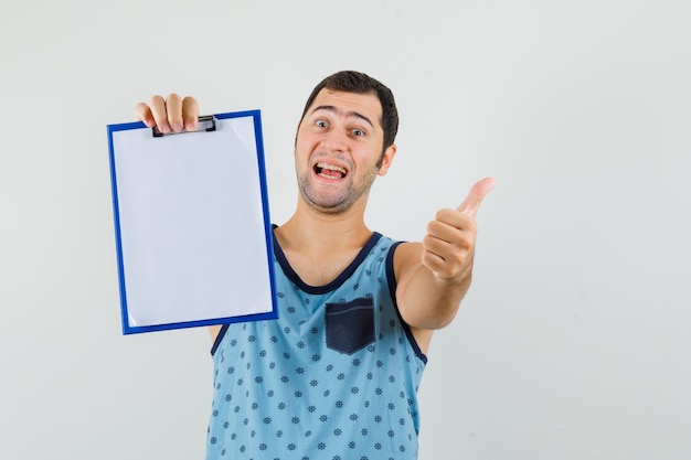 Young man in blue singlet holding clipboard, showing thumb up and looking jovial