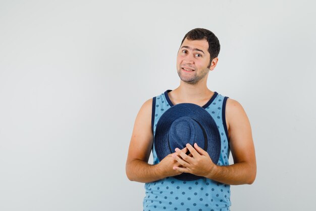 Young man in blue singlet holding hat and looking cheery