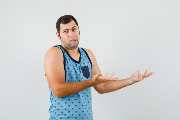 Young man in blue singlet stretching hands aside in puzzled gesture