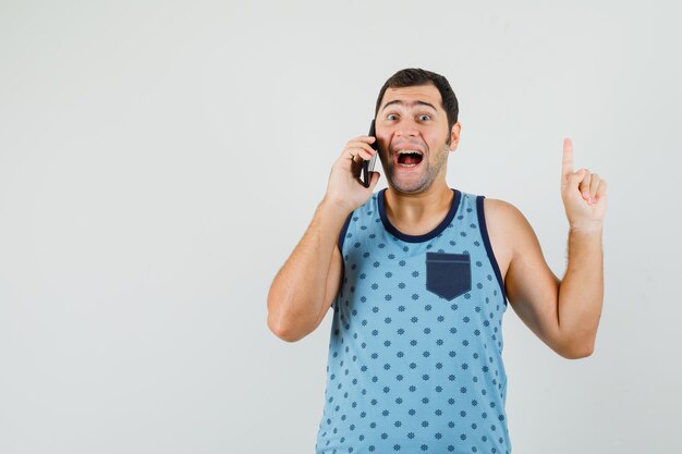 Young man in blue singlet talking on mobile phone, pointing up and looking happy