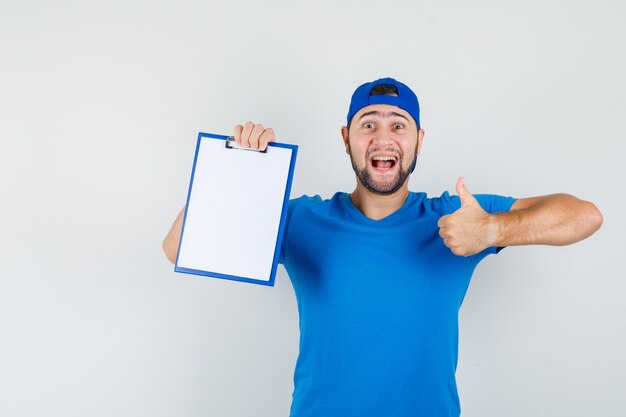 Young man in blue t-shirt and cap holding clipboard with thumb up and looking happy