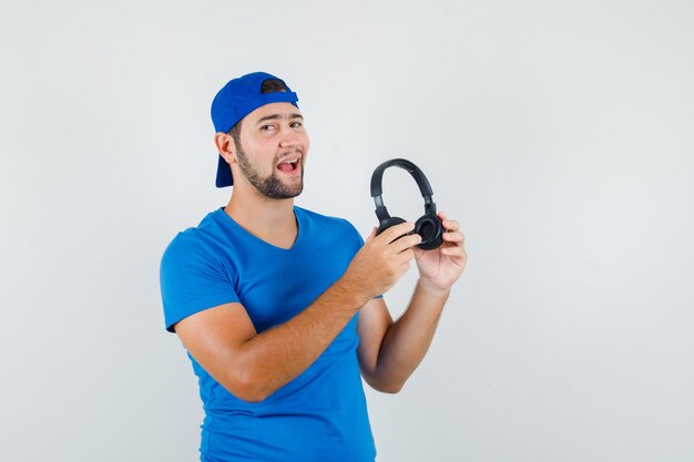 Young man in blue t-shirt and cap holding headphones and looking optimistic