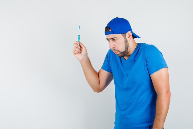 Young man in blue t-shirt and cap holding toothbrush and feeling bad