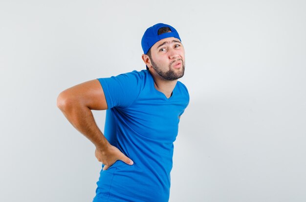 Young man in blue t-shirt and cap suffering from back pain and looking tired